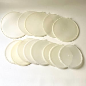 May include: A collection of translucent, off-white plastic lids, arranged in two groups. The lids are round with a slightly raised edge and a small tab for easy removal. The image is well-lit, highlighting the simple design and the material's subtle variations.