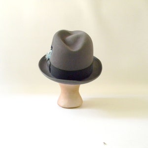 May include: A gray fedora hat with a black band and a small blue feather accent.