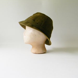 May include: A green bucket hat made of a textured fabric. The hat is sitting on a mannequin head.
