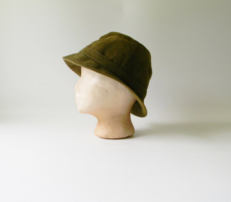 May include: A green bucket hat made of a textured fabric. The hat is sitting on a mannequin head.