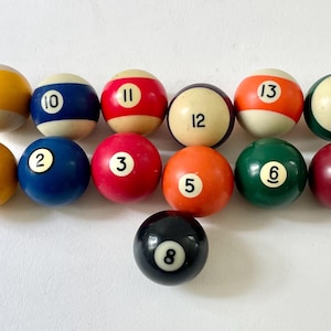 May include: A collection of billiard balls, each with a different color and number. The balls are arranged in a semi-circle, with the black 8-ball in the center. Colors include yellow, blue, red, orange, green, and maroon.