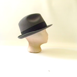 May include: A gray fedora hat with a black band. The hat is on a white mannequin head.