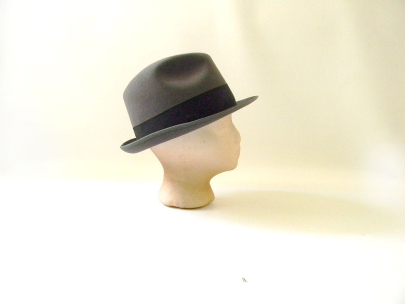 May include: A gray fedora hat with a black band. The hat is on a white mannequin head.