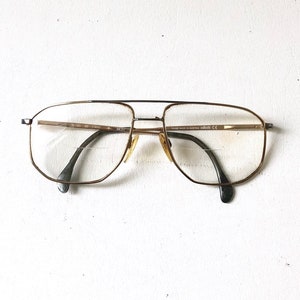 May include: Gold-tone metal eyeglasses with a rectangular frame and clear lenses. The frame has the text "FRAME MADE IN AUSTRIA" and "CE" on the right temple.