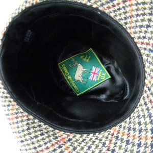 May include: A brown, black, and white tweed hat with a black satin lining. The hat has a label inside that says "Countryside Classics" and "Designed in UK".