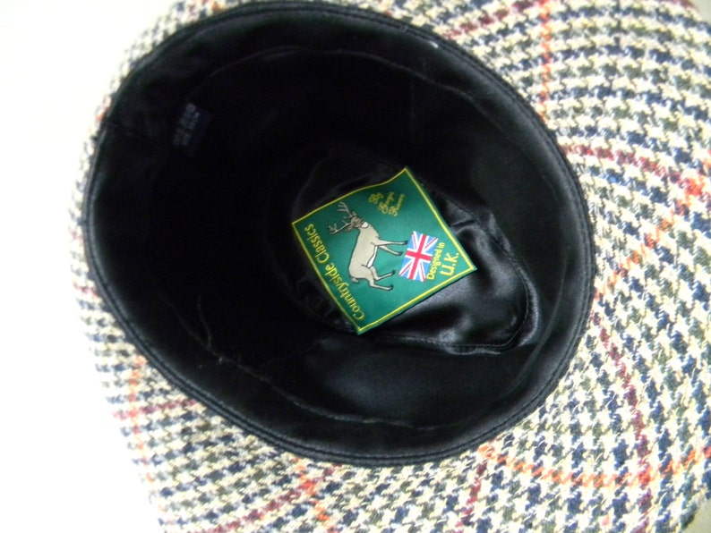 May include: A brown, black, and white tweed hat with a black satin lining. The hat has a label inside that says "Countryside Classics" and "Designed in UK".