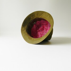 May include: A green and brown hat with a pink lining. The hat is turned inside out, showing the lining.
