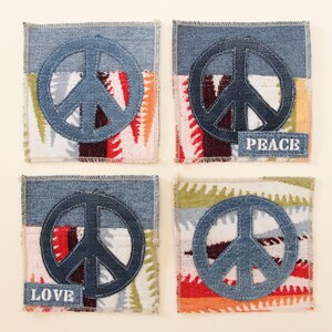 May include: Four square denim coasters with peace signs in the center. The coasters are made of patchwork fabric with different colors and patterns. Two of the coasters have the words "LOVE" and "PEACE" embroidered on them.