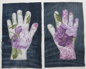 Può includere: Due toppe in tessuto denim, ciascuna a forma di mano. Le mani sono riempite con un motivo floreale nei toni del viola, rosa e verde. I bordi delle mani sono delineati con cuciture bianche.