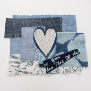 Könnte beinhalten: Ein weißer herzförmiger Patch mit geometrischem Muster ist auf ein Patchwork aus blauem Jeansstoff genäht. Der Stoff ist geschichtet und enthält ein Stück weiße Spitze. Ein blaues Jeansband mit dem Text "then This W Au" ist auf den Stoff genäht.