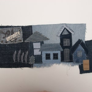 Puede incluir: Una obra de arte de patchwork de mezclilla que representa un pueblo pequeño con casas hechas de diferentes tonos de mezclilla azul. La pieza incluye una pequeña etiqueta con el texto "emonite" en ella.
