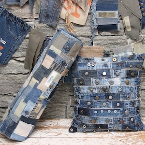 Könnte beinhalten: Zwei dekorative Kissen aus recyceltem Jeansstoff. Die Kissen sind mit Patchwork-Jeansquadraten bedeckt und haben angenähte Metallknöpfe. Die Kissen liegen auf einer Holzoberfläche.