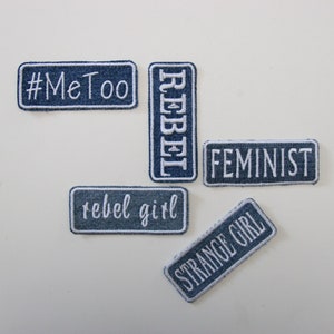 Könnte beinhalten: Eine Sammlung von Denim-Patches mit weiß gesticktem Text. Die Patches enthalten die Phrasen "#MeToo", "REBEL", "FEMINIST", "rebel girl" und "STRANGE GIRL". Die Patches sind rechteckig mit weißem Rand.
