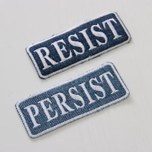 Puede incluir: Dos parches de mezclilla azul con texto bordado en blanco. El parche superior dice "RESIST" y el parche inferior dice "PERSIST".