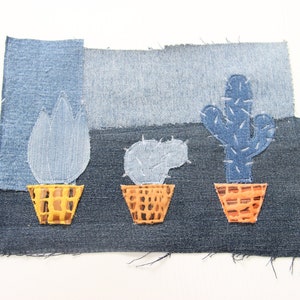 May include: Three denim cactus plants in orange pots on a denim background. The cactus plants are made from denim fabric and have been stitched together.