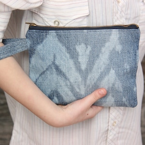 May include: A blue denim clutch bag with a zipper closure and a matching strap. The bag has a tie-dye pattern.
