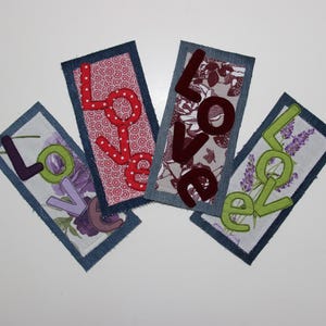 Peut inclure: Quatre marque-pages en tissu avec le mot "LOVE" écrit en différentes couleurs et motifs. Les marque-pages sont en jean et présentent une variété de tissus avec des motifs floraux et géométriques.