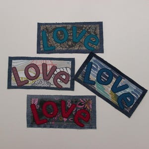 Può includere: Quattro toppe di jeans con la parola "LOVE" ricamata in diversi colori e motivi. Le toppe sono in tessuto denim con diversi motivi e colori. La parola "LOVE" è ricamata in blu, rosa, rosso e blu.