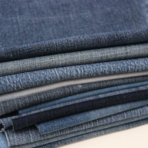 Puede incluir: Una pila de tela vaquera azul de diferentes tonos. La tela está doblada y superpuesta, mostrando las diferentes texturas y tejidos.