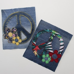 May include: Two denim patches with peace signs embroidered on them. One peace sign is surrounded by colourful flowers and the other is surrounded by tropical leaves.