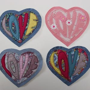Könnte beinhalten: Vier herzförmige Aufnäher. Drei haben das Wort "LOVE" in farbenfrohem Stoff vor einem Jeanshintergrund. Ein rosa Herz hat das Wort "LOVE" in Weiß mit kleinen Blumenakzenten genäht. Diese Aufnäher sind für Bastelarbeiten geeignet.
