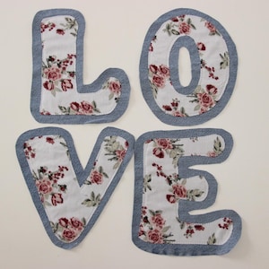 Op de afbeelding: Het woord "LOVE" gespeld in grote, blauwe denim letters met een witte bloemenstof achtergrond.