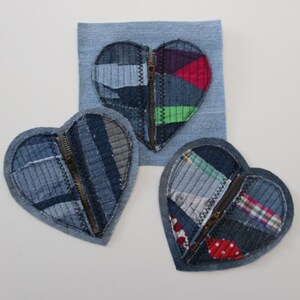 Puede incluir: Tres parches de tela en forma de corazón cosidos juntos con cremalleras. Cada parche está hecho de diferentes telas de mezclilla en tonos de azul, verde, rojo y blanco.