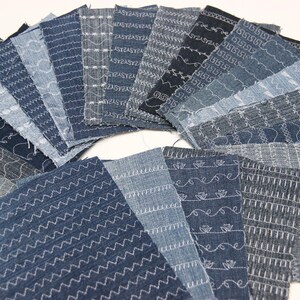 Op de afbeelding: Een verzameling denim stofstalen met verschillende steekpatronen. De stalen zijn in een waaier vorm gerangschikt, met de steken zichtbaar op de voorkant van elk stuk.