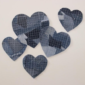 May include: Five blue denim patchwork heart shapes, each with a different pattern and size, are arranged on a white background.