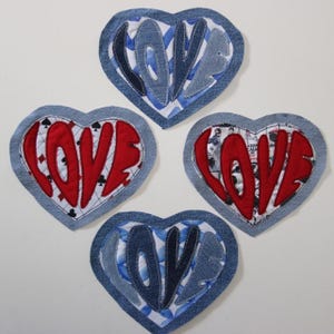 Puede incluir: Cuatro parches de tela en forma de corazón con bordes de mezclilla. Cada parche muestra la palabra "LOVE" en un color contrastante. Dos parches tienen letras "LOVE" azules y dos rojas. Un parche rojo tiene símbolos de picas negras.