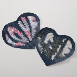 Könnte beinhalten: Zwei herzförmige Patches aus Denim mit dem Wort "LOVE" in rosa und weißer Tarnfarbe gestickt.