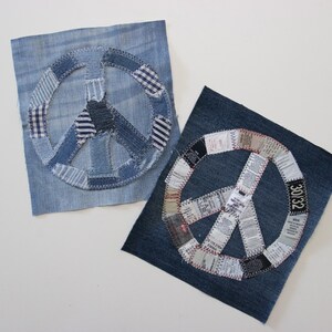 May include: Two denim peace signs made from fabric scraps. The peace signs are stitched together with white thread. The peace sign on the left is on a blue denim background. The peace sign on the right is on a dark blue denim background.