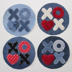 Op de afbeelding: Vier denim-onderzetters met verschillende stoffen ontwerpen. Elke onderzetter heeft een hart, een cirkel en een X en O. De ontwerpen omvatten rode, witte, zwarte en grijze stoffen.