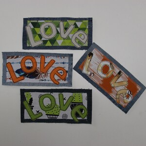 Puede incluir: Cuatro parches de tela con la palabra "LOVE" escrita en diferentes colores y patrones. Los parches son todos rectangulares y tienen un borde de mezclilla.