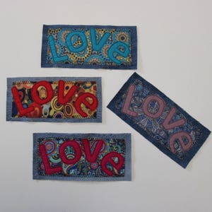 Peut inclure: Quatre patchs en denim avec le mot "LOVE" appliqué en différentes couleurs. Les patchs ont des fonds à motifs variés, notamment des motifs floraux et cachemire. Les lettres sont dans des tons de bleu, de rouge et de rose.