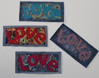 Può includere: Quattro toppe in denim con la parola "LOVE" applicata in diversi colori. Le toppe hanno una varietà di sfondi a fantasia, tra cui disegni floreali e paisley. Le lettere sono in tonalità di blu, rosso e rosa.