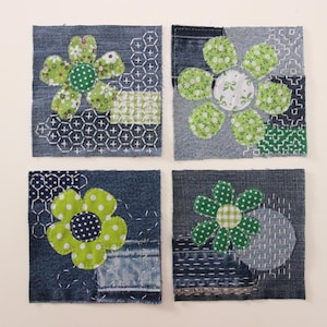 May include: Four denim squares, each featuring a different appliqued flower design. The flowers have green petals and contrasting centres. The denim is a medium wash, with decorative stitching and patchwork details, giving a handcrafted feel.
