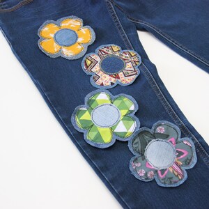 Puede incluir: Vaqueros azules de denim con cuatro parches de flores de colores cosidos. Los parches están hechos de diferentes telas y patrones.