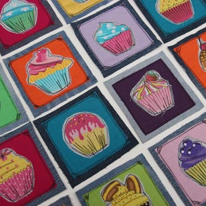 Può includere: Una collezione di 12 applicazioni di cupcake in tessuto colorato, ognuna con un design e una glassa diversi, disposte su uno sfondo di jeans.