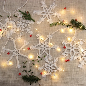 May include: White crocheted snowflakes with fairy lights and red berries on a hessian background.