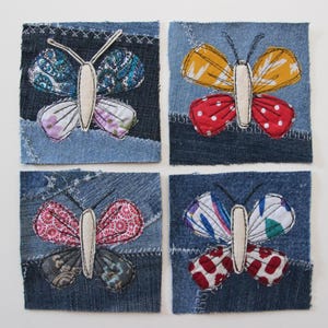 Puede incluir: Cuatro cuadrados de mezclilla con mariposas bordadas. Cada mariposa está hecha de diferentes telas estampadas y tiene un cuerpo blanco. Las mariposas son de color rojo, amarillo, azul y rosa.