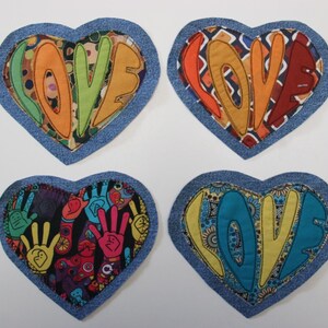 Op de afbeelding: Vier hartvormige stoffen patches met het woord "LOVE" in verschillende kleuren. Elke patch heeft een denimblauwe rand. De letters "LOVE" zijn in groen, oranje en geel, met patronen.