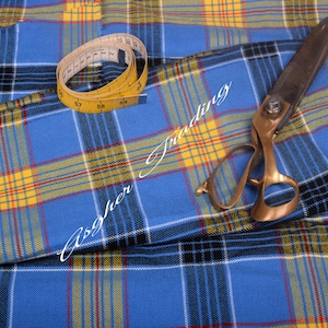May include: Blue, yellow, and black plaid fabric with a yellow measuring tape and large scissors. The fabric has a repeating pattern of intersecting lines. The measuring tape is yellow with black markings. The scissors are bronze-colored.