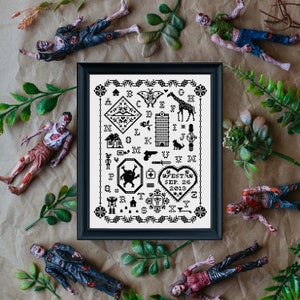 May include: A framed black and white cross-stitch sampler with various motifs, including a giraffe, house, and heart with the text "EST. SEP. 26 2013." The frame is surrounded by toy zombies and greenery.