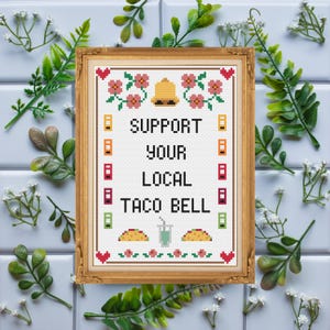 Puede incluir: Un diseño de punto de cruz enmarcado con el texto "SUPPORT YOUR LOCAL TACO BELL". El diseño presenta una campana dorada, flores rosas y elementos de borde coloridos. El marco es dorado y el fondo es blanco.