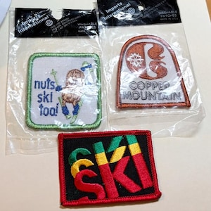 May include: Three embroidered patches. One square patch features a brown squirrel skiing with the text 'nuts ski too!'. One arched patch displays a copper-colored logo and the text 'COPPER MOUNTAIN'. One rectangular patch features the word 'SKI' in red, yellow, and green.