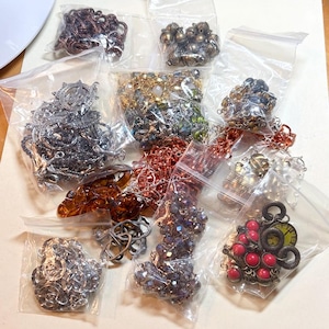 May include: Assortment of jewelry-making supplies in clear plastic bags. Includes various metal chains, beads, and decorative elements in silver, bronze, copper, and other colors. Ideal for crafting necklaces, bracelets, and earrings.