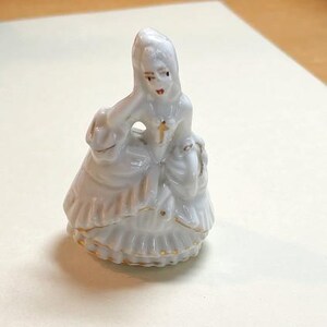 May include: White porcelain figurine of a woman in a gown with gold accents. The figurine is wearing a crown and has a delicate facial expression.