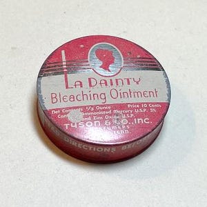 May include: A vintage La Dainty Bleaching Ointment tin with a red and silver design. The tin's label includes the text "La Dainty Bleaching Ointment," the net contents of 1/3 ounce, and the price of 10 cents. The manufacturer is Tyson & Co., Inc.