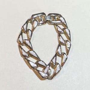 May include: A gold chain bracelet with white enamel accents. The bracelet is made of a thick, chunky chain with a clasp closure.
